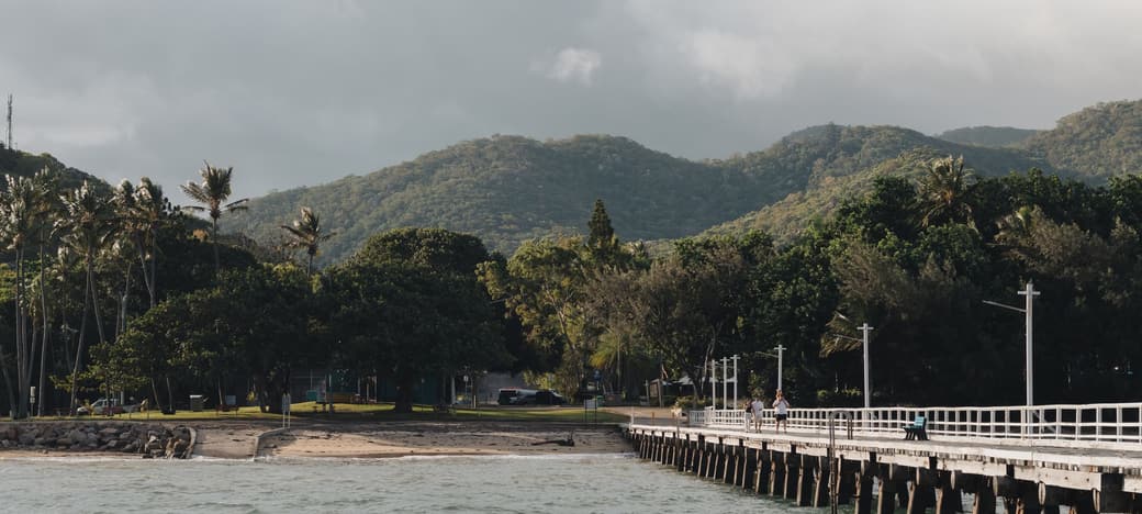 The coastline near Cairns, with a jetty running out over the water and rainforest ranges behind